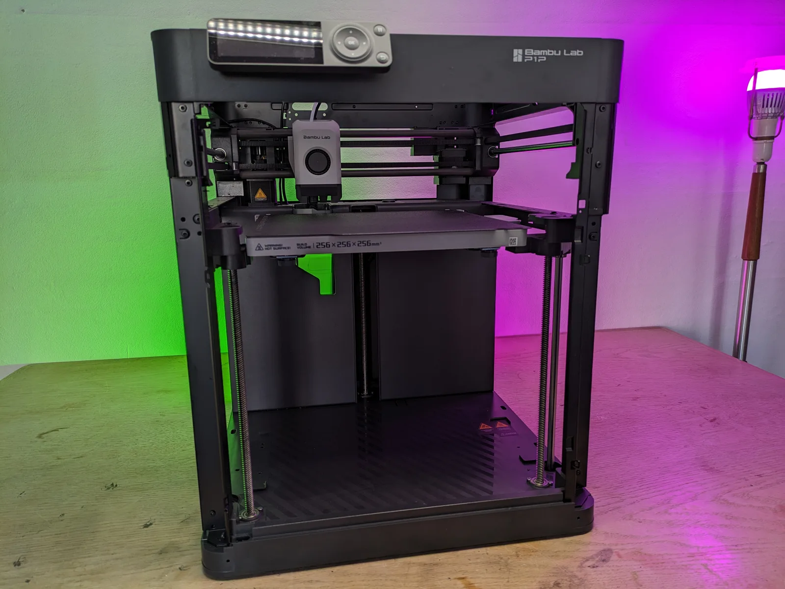 Bambu Lab P1P front view, lid-off open frame revealing the toolhead, ambient green and pink lighting