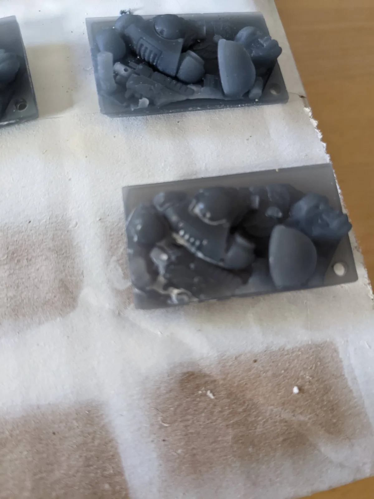 Two freshly washed dark grey resin scenic bases resting on white kitchen paper, surface still wet from isopropyl alcohol