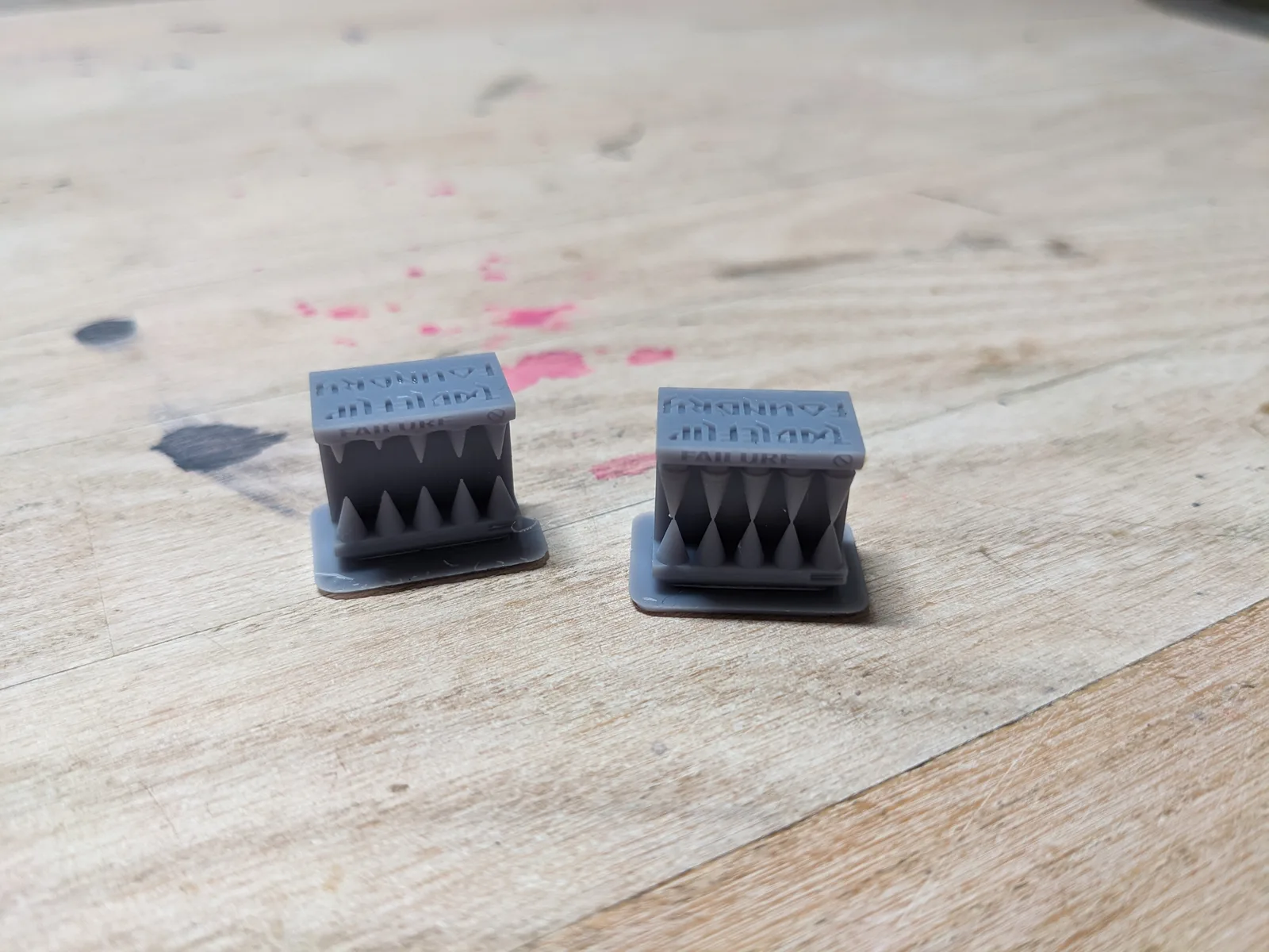 Two identical grey resin Cones of Calibration v1 side by side on a light wooden surface, each a rectangular block with triangular spike teeth and embossed MICRON MONSTER and FAILURE text on top, printed at 35 microns on an Elegoo Mars 3 Pro