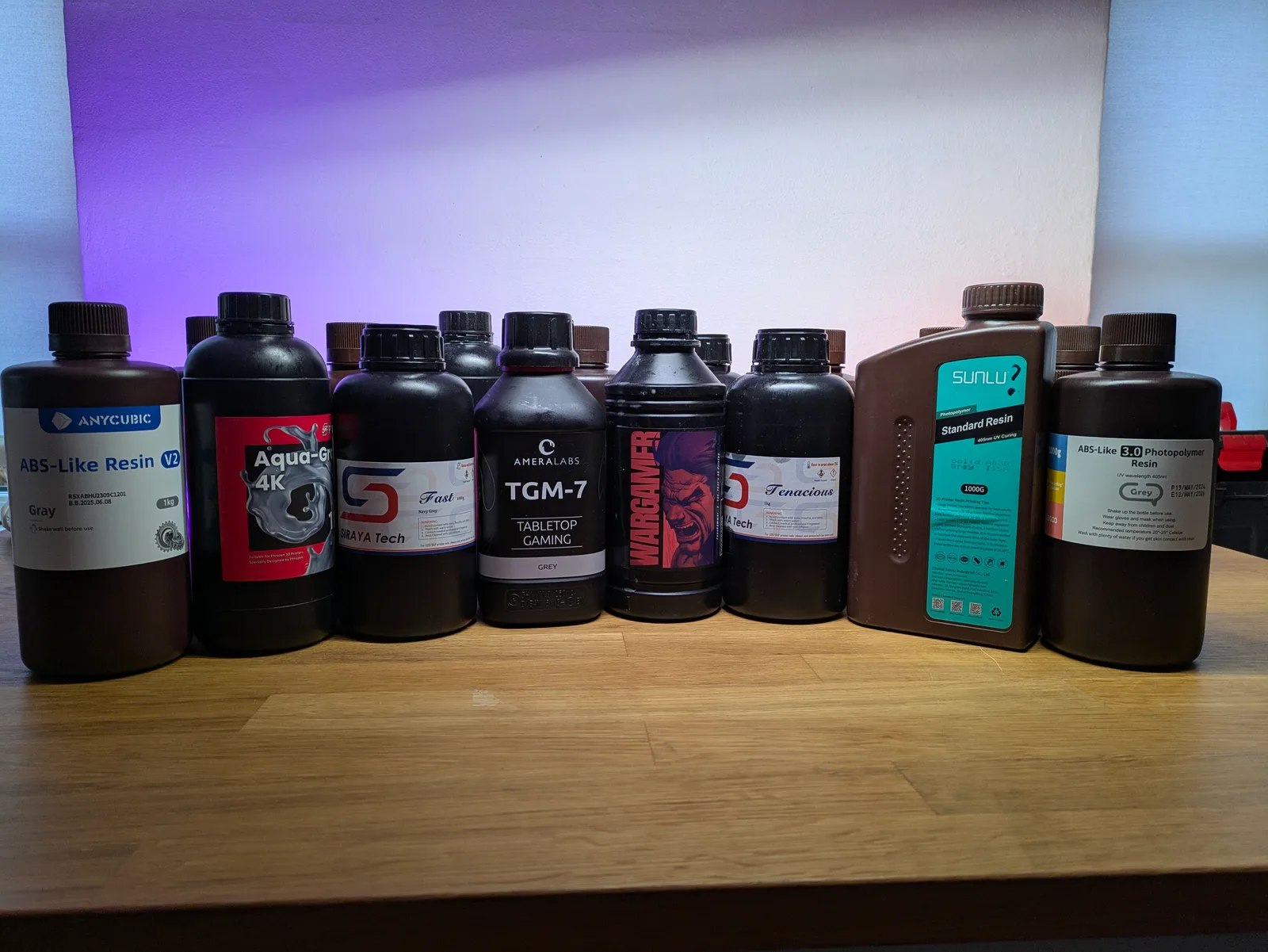 Eight grey resin bottles in a row on a shelf, showing different brands and sizes of standard miniature printing resin