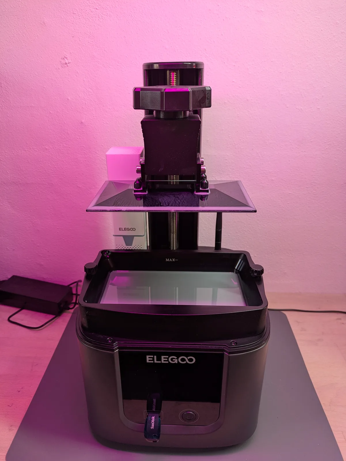 Mars 4 Ultra printer mid-setup with lid off, resin in the vat, build plate raised with a small test cube attached, and a SanDisk SD card in the front slot, ready to run a calibration print