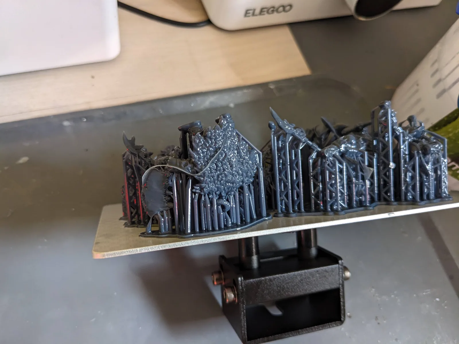 Freshly printed build plate of dark grey fantasy miniatures still on lattice supports, wash and cure station blurred behind