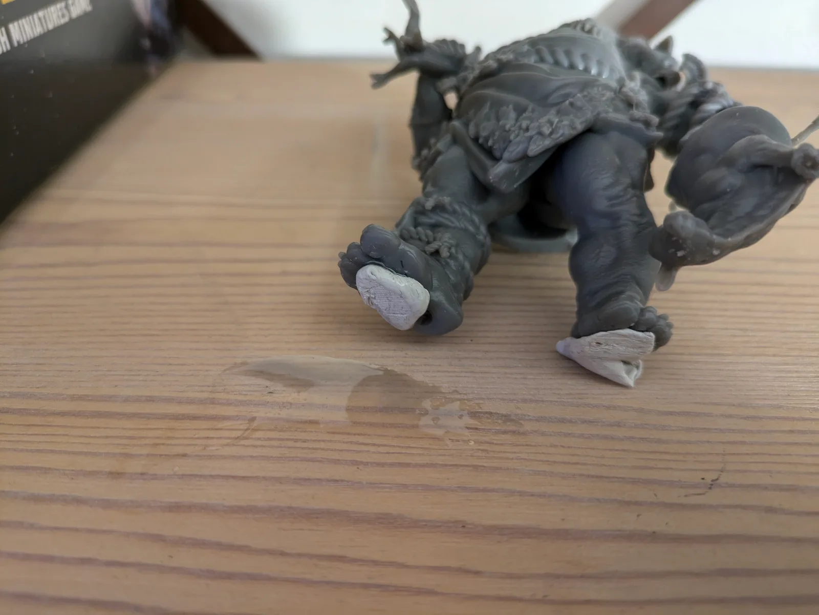 Large dark grey resin monster figure lying on its side on a wooden surface with a pool of uncured liquid resin visible where an internal hollow void cracked through at the foot area, exposing lighter grey interior