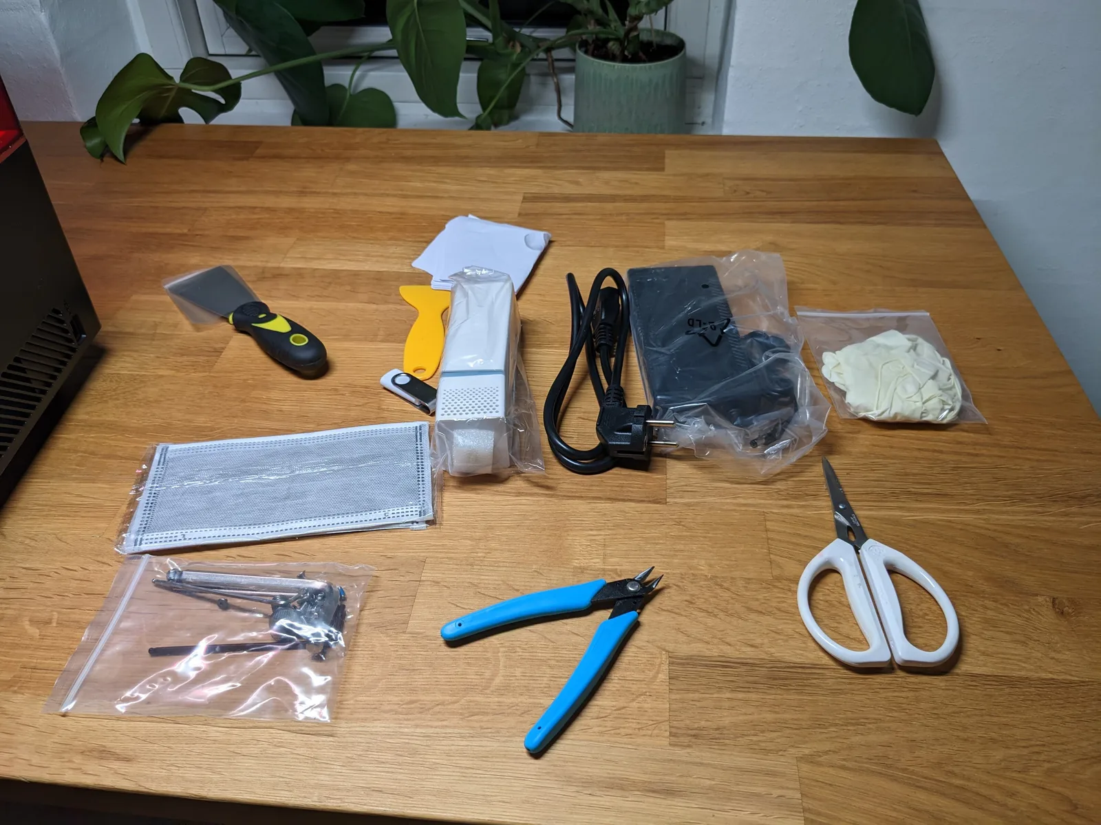 Saturn 2 in-box accessories laid flat on a wooden table: grey metal scraper, yellow plastic scraper, FEP films, allen key bag, EU power brick, blue flush cutters, scissors, white latex gloves
