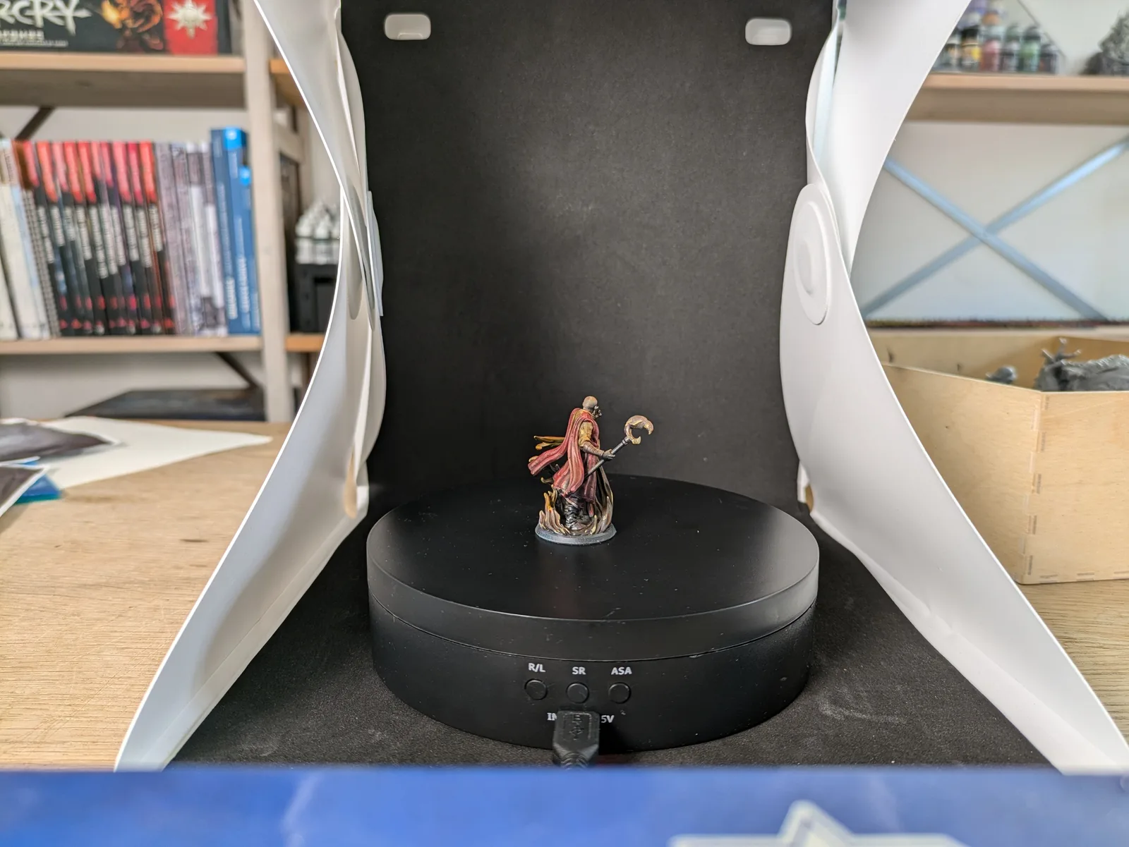 Painted Flesh of Gods Lord Mage of the Ashen Eagle miniature, a bald wizard in brilliant red robes with gold accents holding a crescent tipped staff above a fire effect base