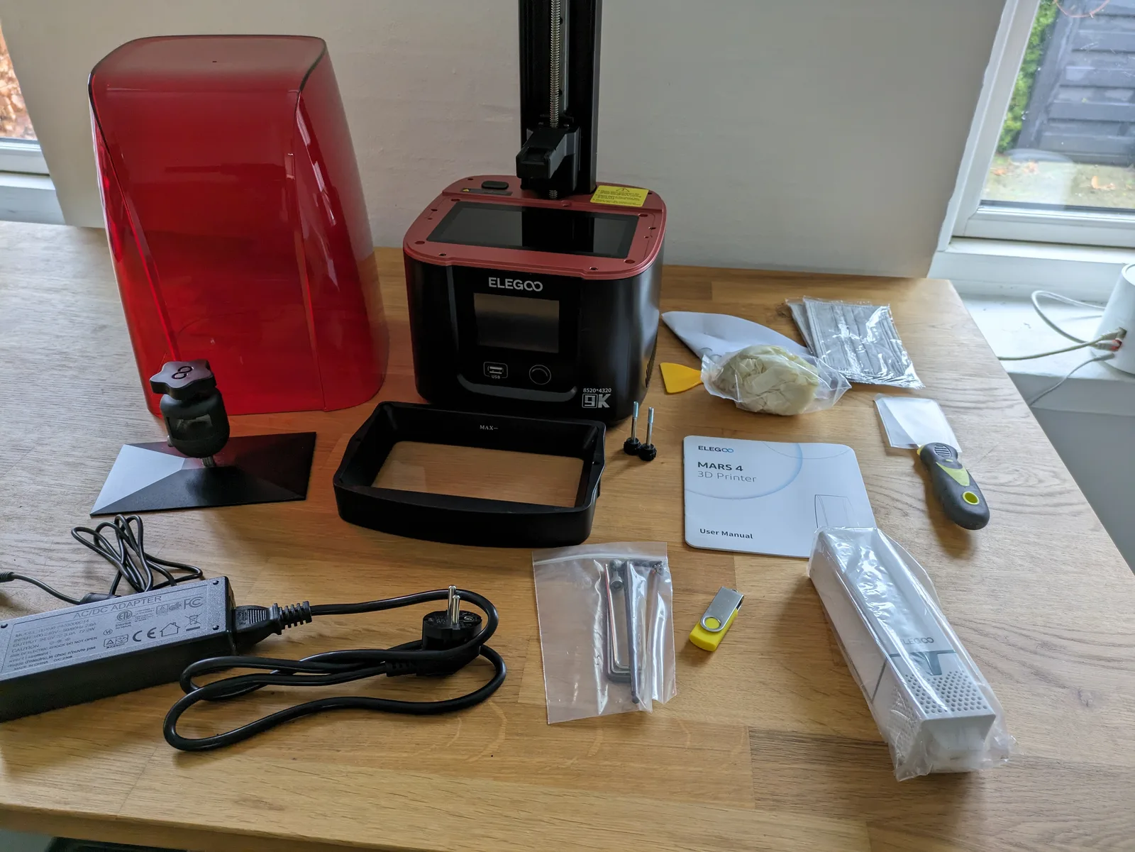 Elegoo Mars 4 laid out on a workbench with its resin vat frame, power adapter, manual, FEP film, allen keys, USB drive and scraper