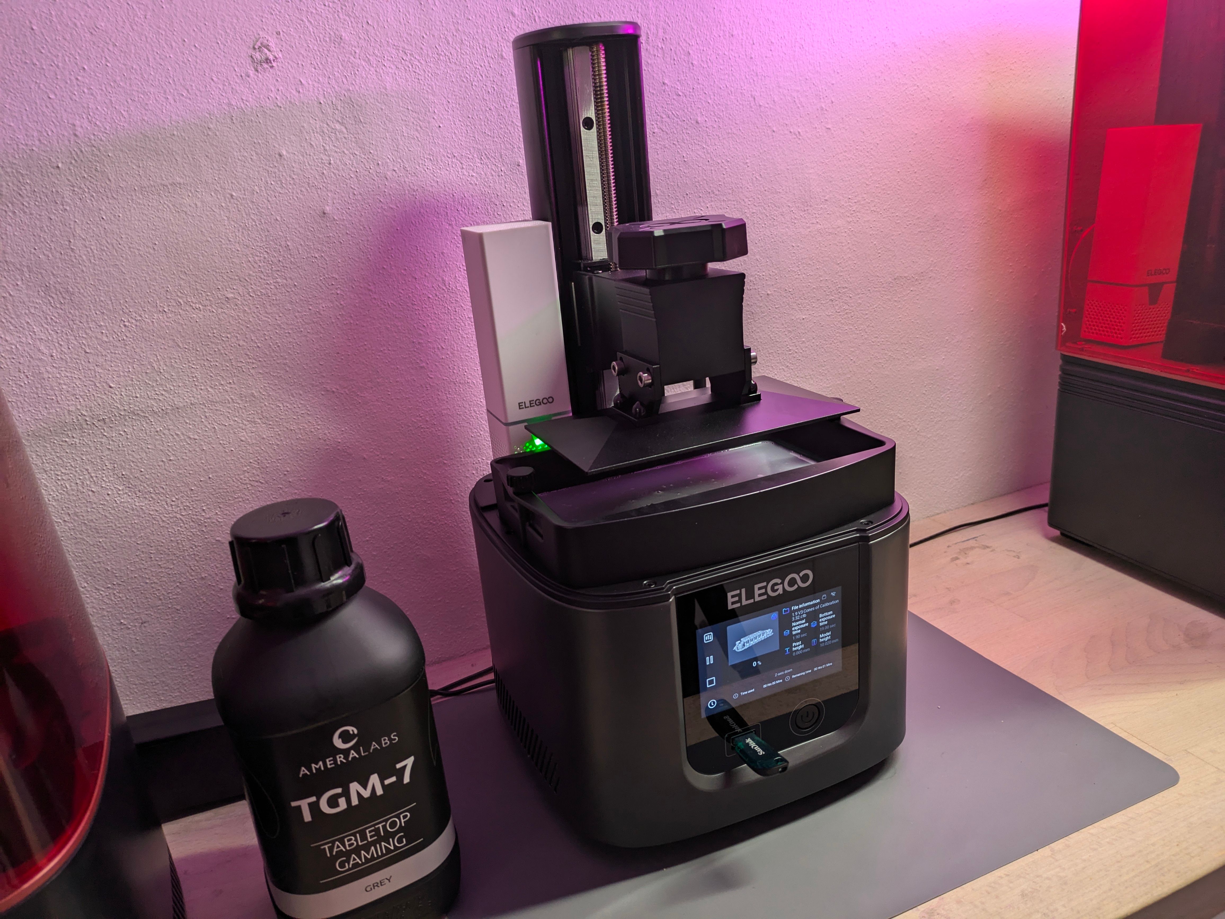 Elegoo Mars 4 resin printer on a workbench beside a black AmeraLabs TGM-7 resin bottle, USB stick in the side port, touchscreen active