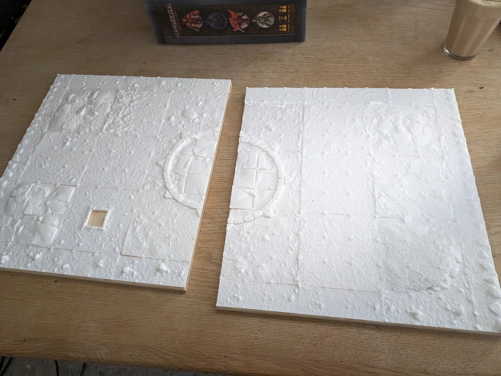 Two square white PLA modular dungeon floor tiles, embossed stone-tile pattern, side by side on a wooden table