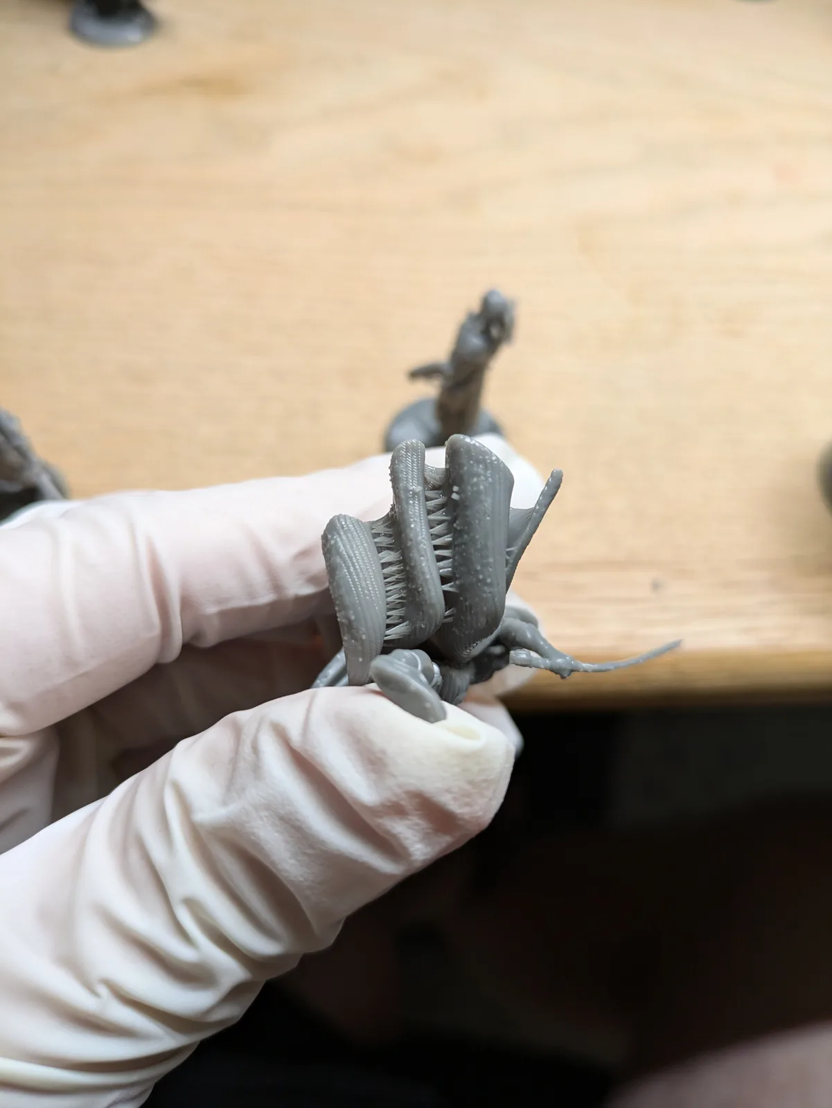 White gloved hand holding a grey resin print that has fused and collapsed, with deformed wings and blobs of over cured resin