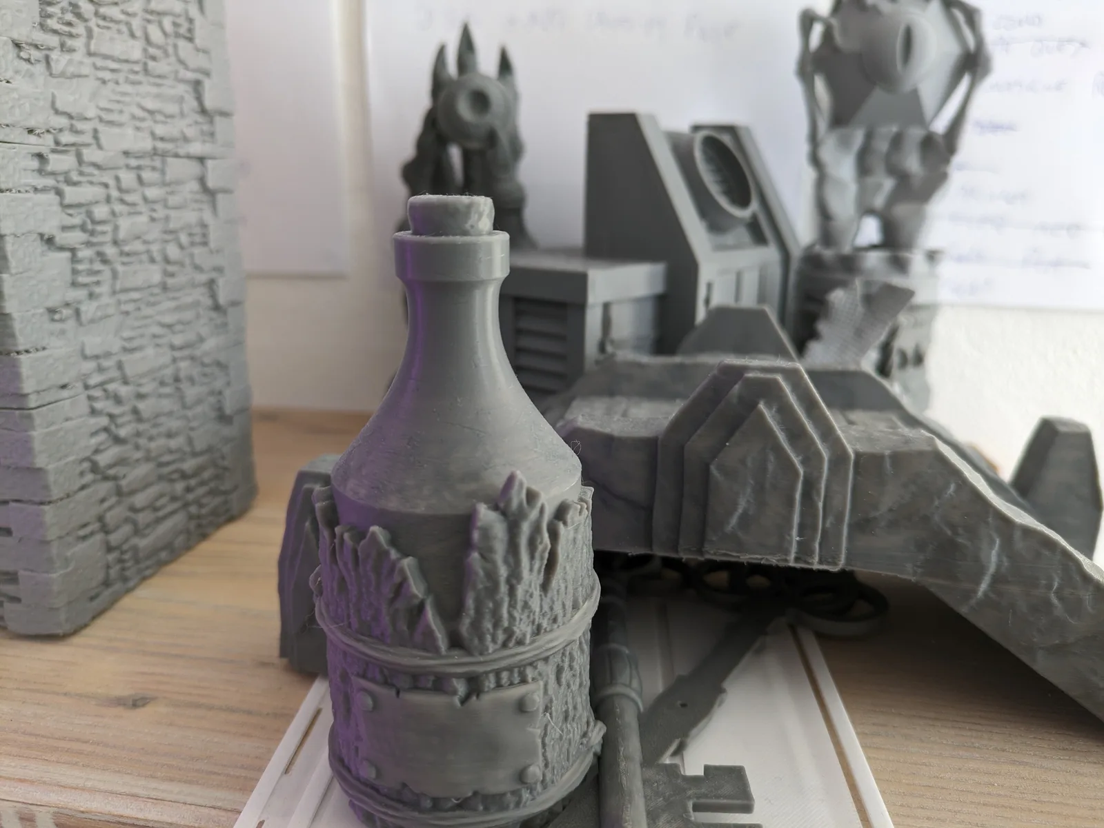 Group of grey PLA terrain pieces printed on a Bambu Lab P1P, ranging from a rune-banded barrel to a brick wall section and a sci-fi gun emplacement