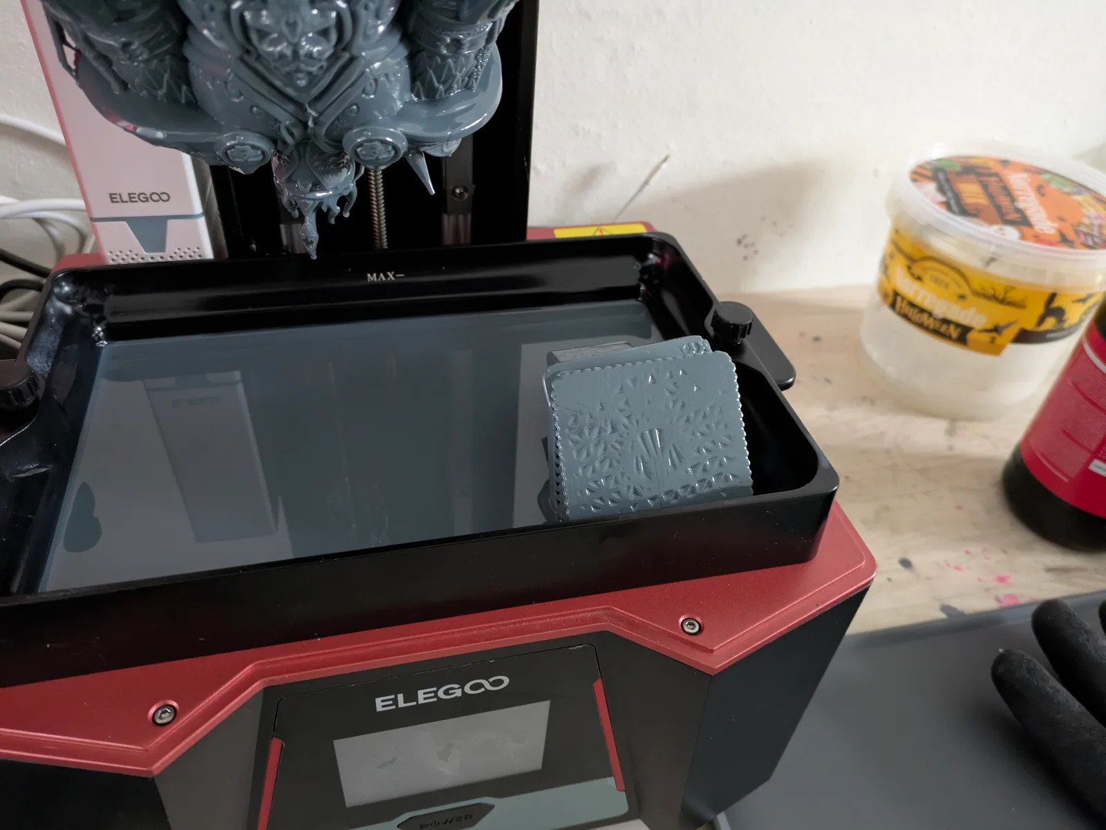 Open Elegoo printer from the front with build plate raised showing a large dark grey complex resin print still attached at the top, while a grey rectangular tile sits flat on the vat bed below, a partial detachment failure