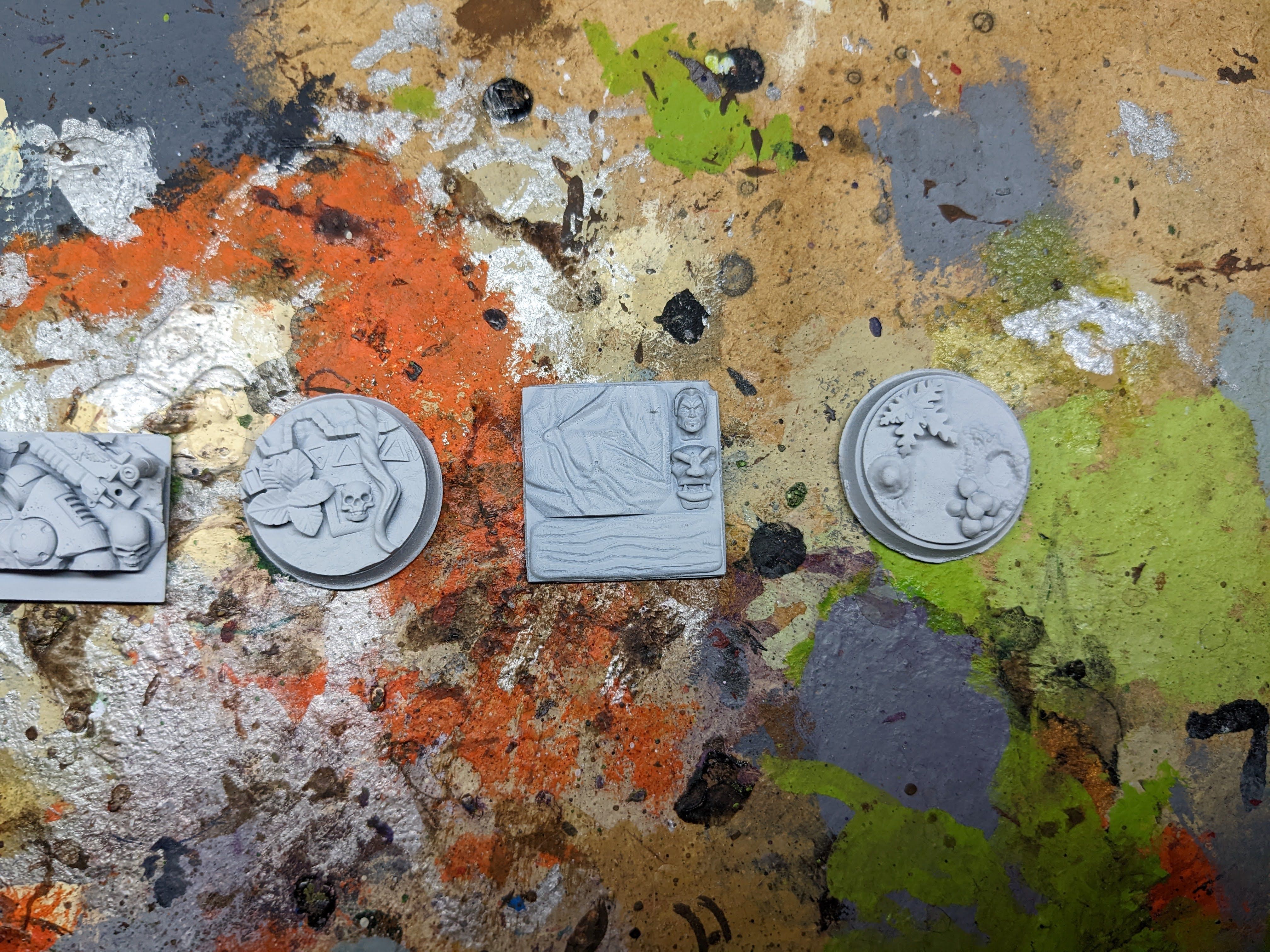 Four grey resin scenic bases on a paint stained palette showing the detail level resin holds at small terrain scale