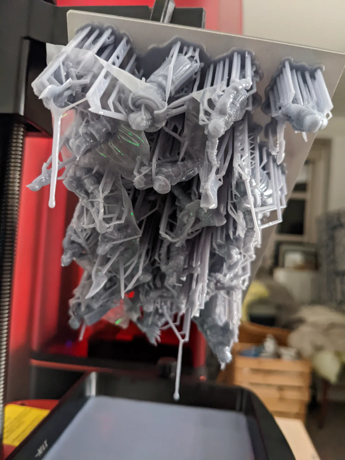 Elegoo Saturn build plate lifted clear of the vat showing a full batch of white resin miniatures on supports, liquid resin dripping from the tips