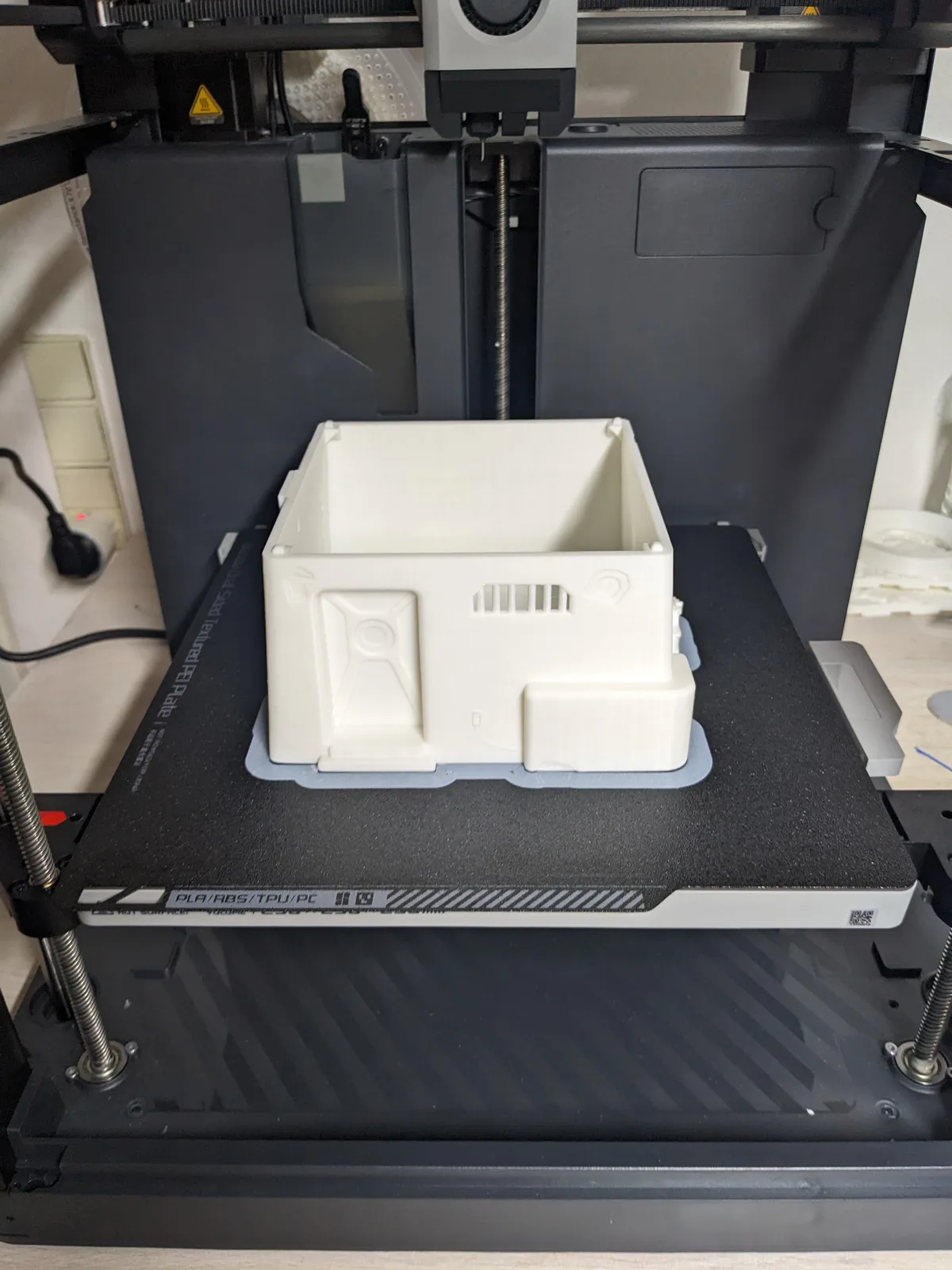 White PLA sci-fi scenic crate freshly printed on a Bambu Lab P1P, build plate visible at the bed front
