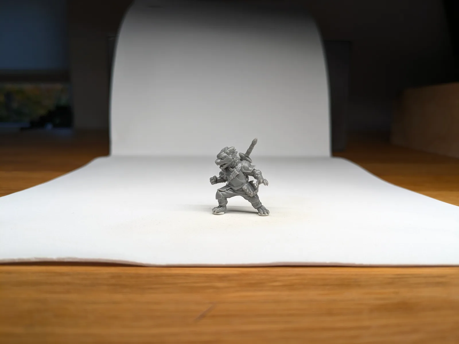 Single grey resin feline reptilian warrior in a wide combat stance drawing a sword from a behind head scabbard, on a white paper sweep