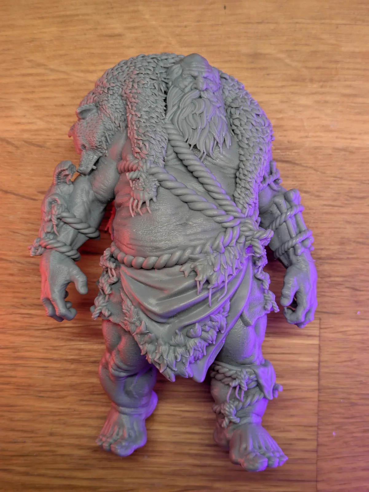 Large grey resin Thorvon Stonehill miniature laid flat on a wooden surface, overhead view showing the dreadlocked mane, rope loincloth, clawed hands, and textured muscled torso