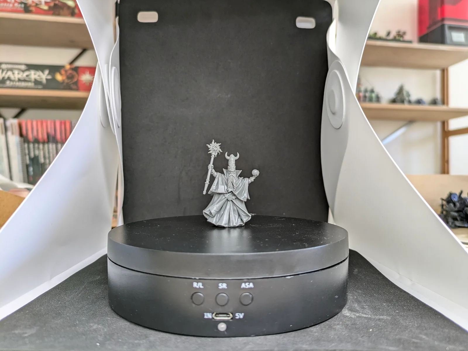 Tall grey resin robed mage on a black rotating turntable in a white and black lightbox, horned helmet, massive voluminous robes with detailed folds, one arm raised holding a celestial sunburst staff